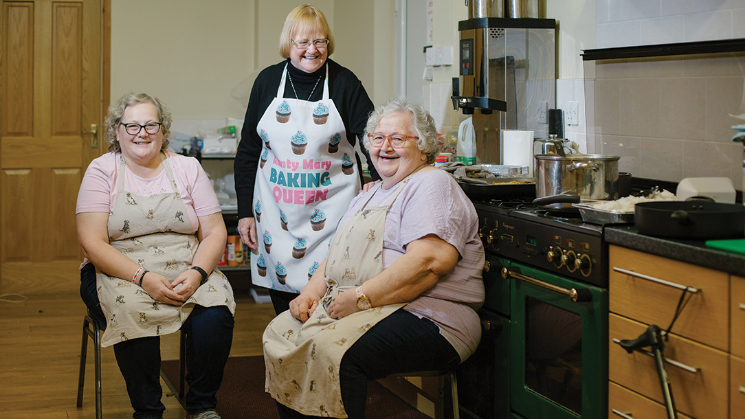 Iris, Mary and Amanda photographed inside a kitchen wearing their aprons.