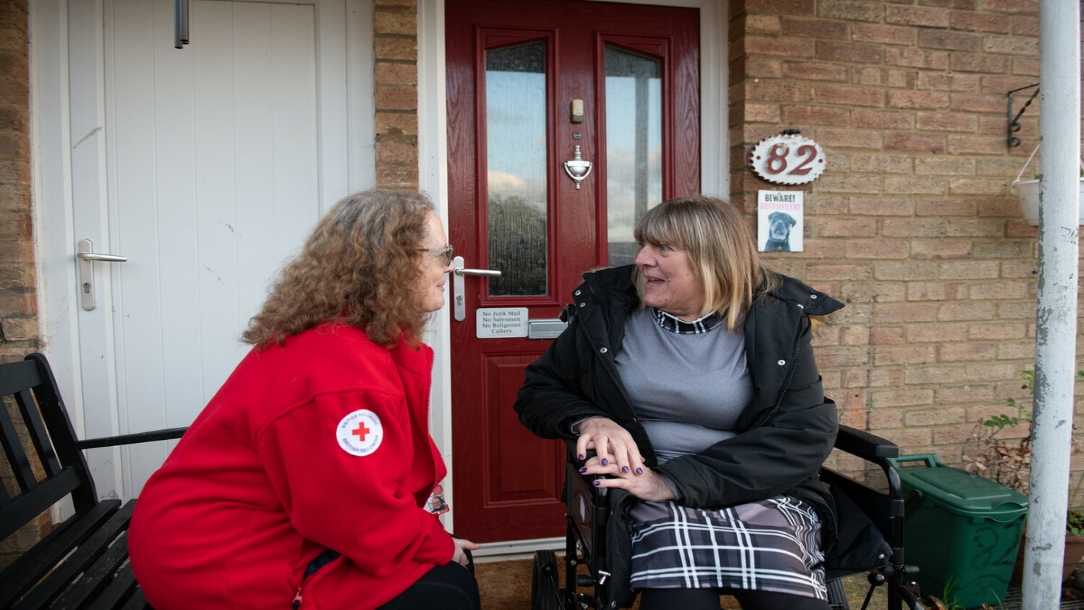 British Red Cross volunteer offers comfort to a lady in a wheelchair.