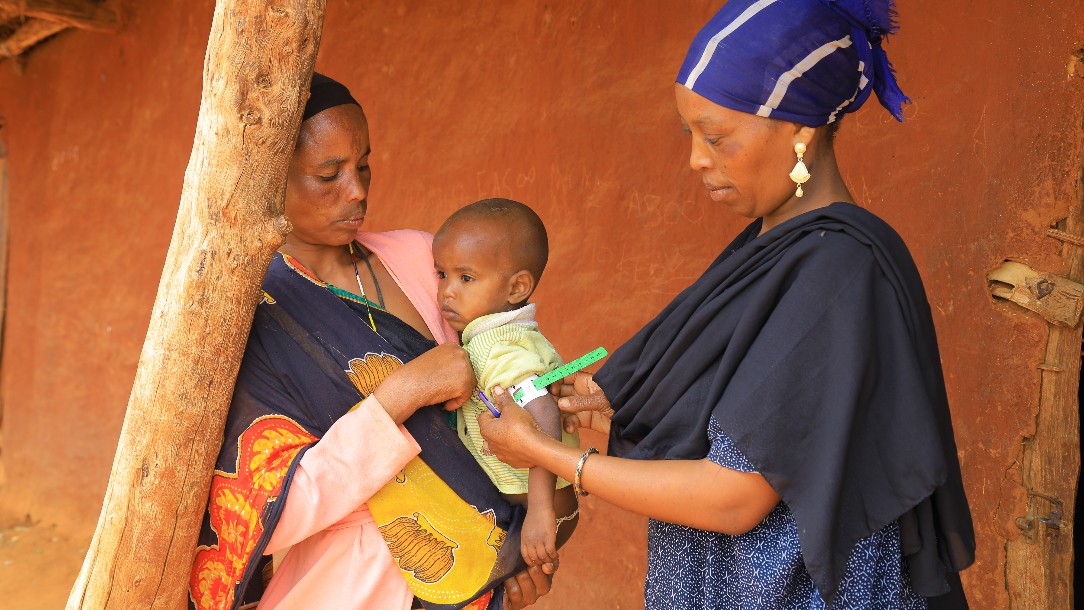 A mother, Loko H, holds her son, Hordola, 2, while a Red Cross community health worker, Loko S, measures the child's arm
