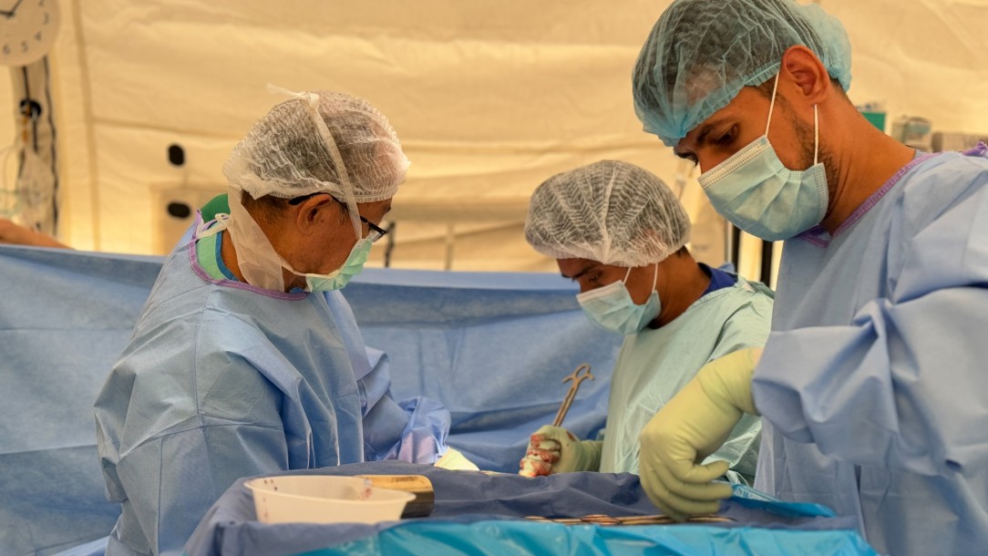 Three surgeons in scrubs operate on an unseen person at the field hospital in Rafah, Gaza