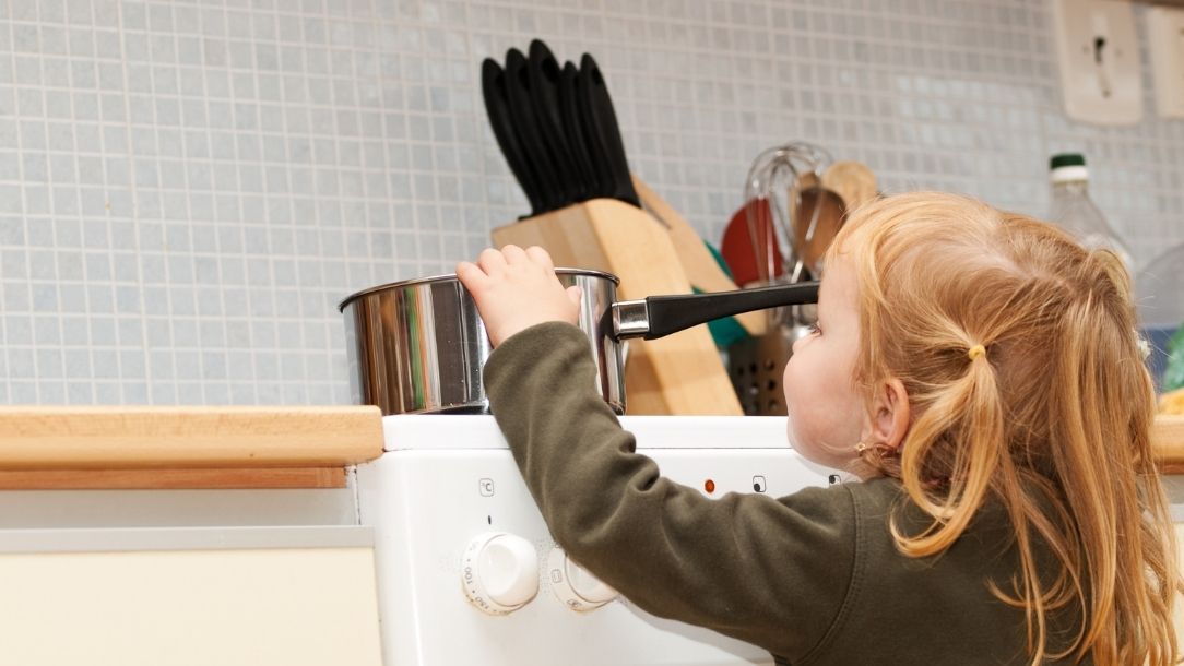 A little girl about to pull a hot saucepan off the stove and is in danger of burning herself.