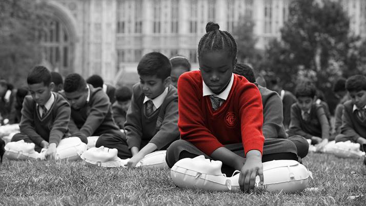 School children participate in a first aid skills lesson outside.