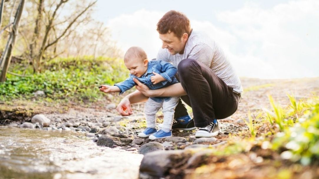 A man and a baby look at something in a stream on a family day out