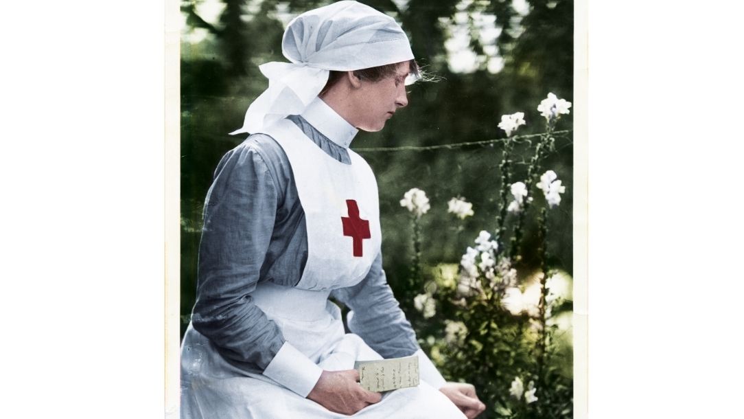 A British Red Cross nurse from the first world war holds a letter and looks thoughtful in a garden.