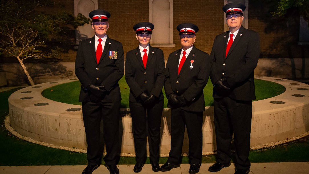 Four British Red Cross volunteers in their ceremonial uniforms look to the camera, stood against a backdrop of a stately garden