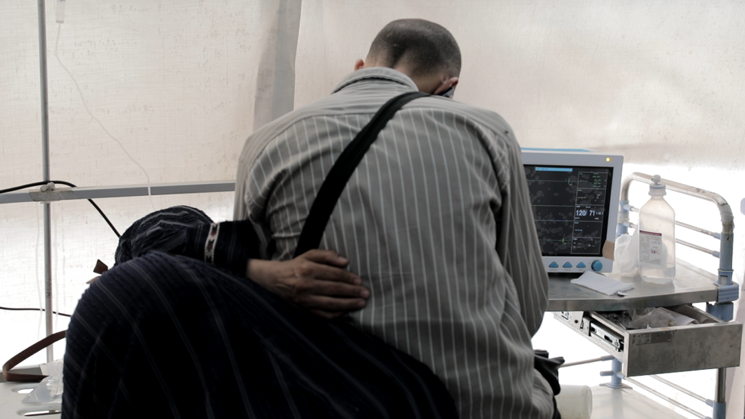 A patient is comforted by a loved one whilst receiving treatment at the Palestine Red Crescent Society Al-Saraya field hospital in Gaza, 31 July 2025