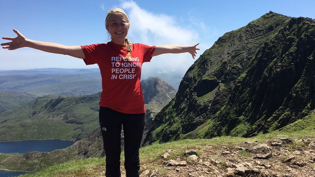 Lady standing at the top of a mountain.