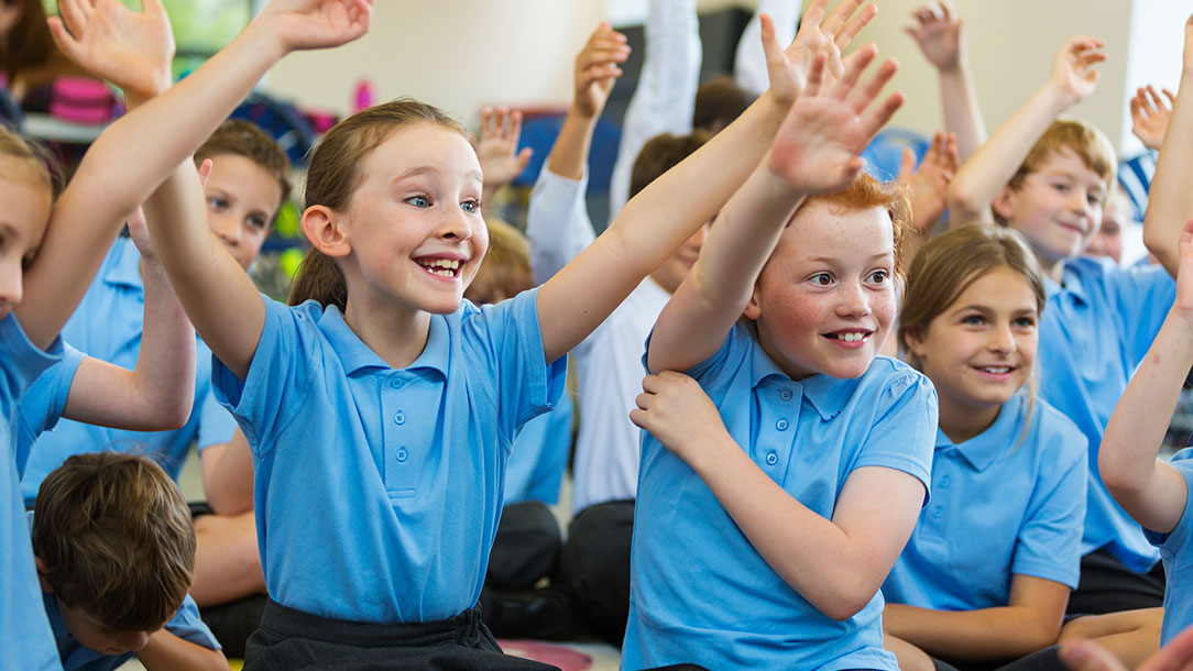 Children in class with their hands up.