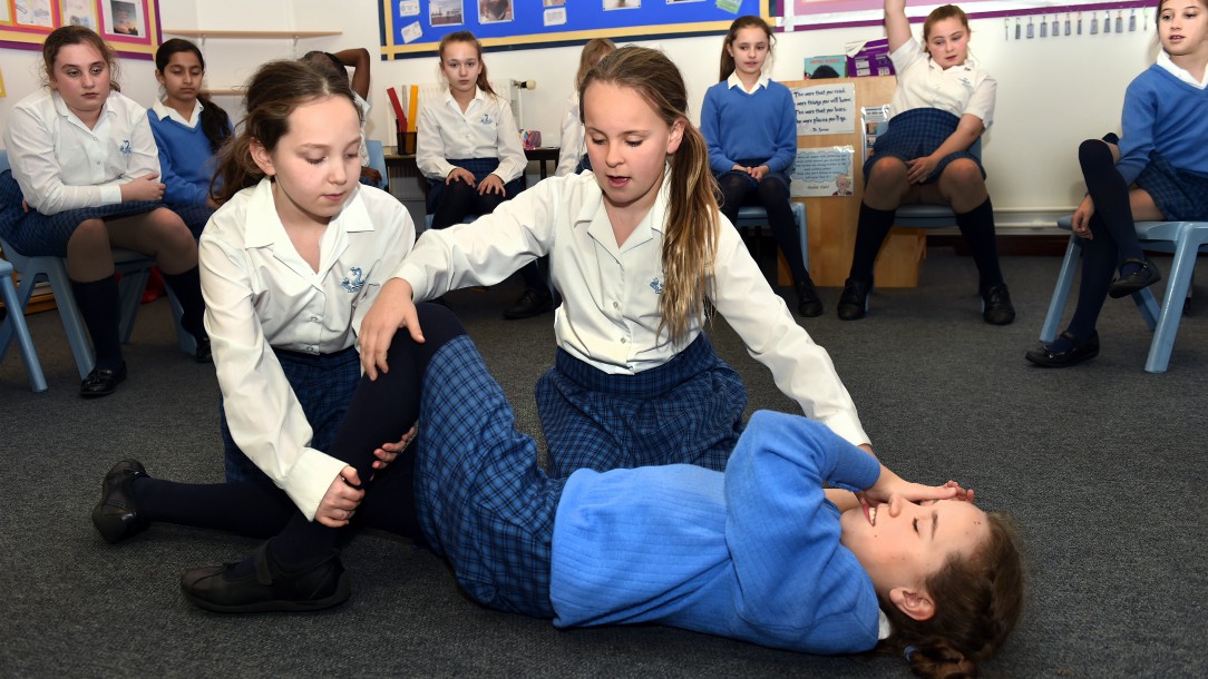 Children in a classroom practise first aid for someone who is unresponsive, using British Red Cross teaching resources.