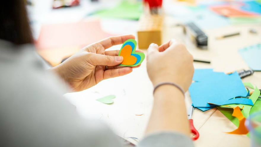 A close-up of a young woman's hands holding cut-out paper hearts in different colours and sizes.