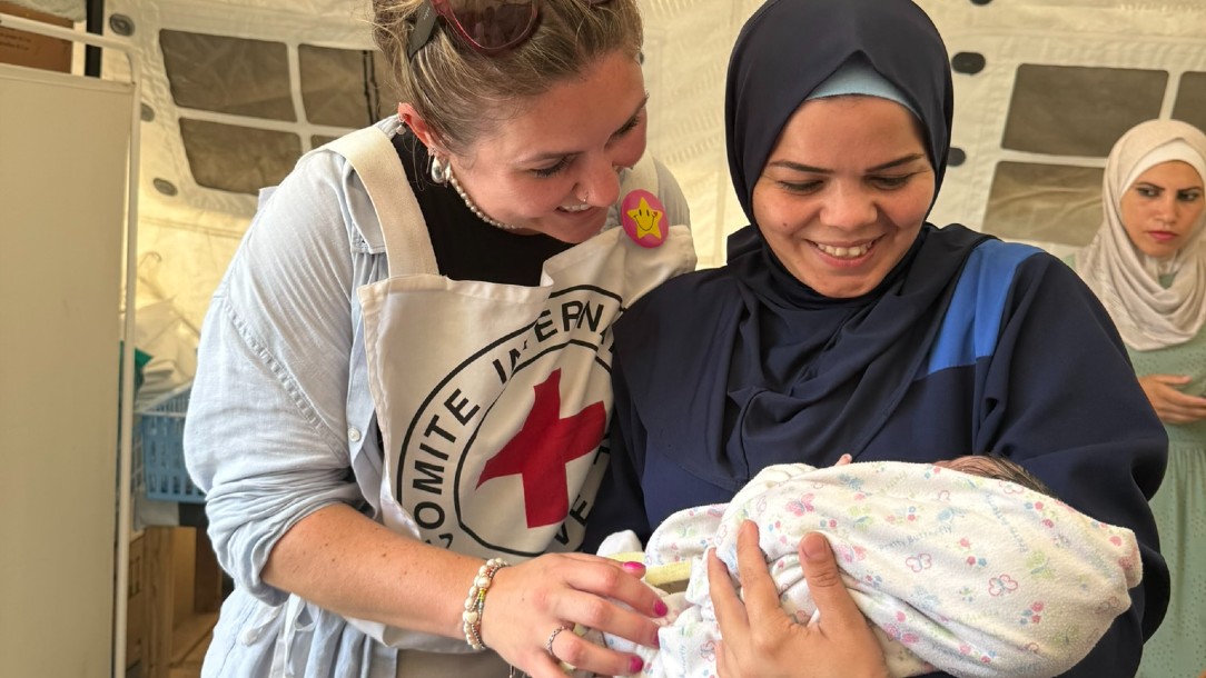 Ghada holds her baby daughter Asia at the Red Cross field hospital in Gaza, while an IFRC worker smiles at the baby