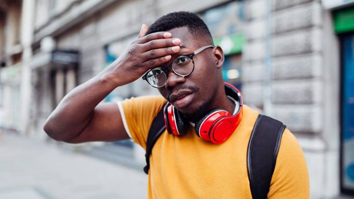 A young man stands in an urban area looking frazzled in a heatwave.