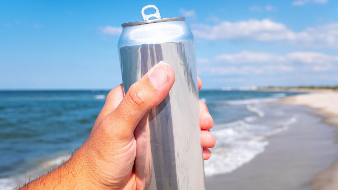 Someone holding beer aloft on a sunny beach.