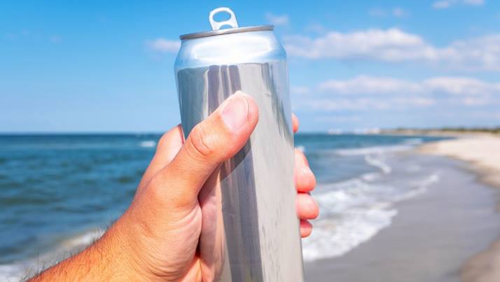 Someone holding beer aloft on a sunny beach.