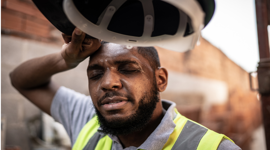 Close-up shot of a male construction worker wiping the sweat from his forehead with his arm while holding his construction hat