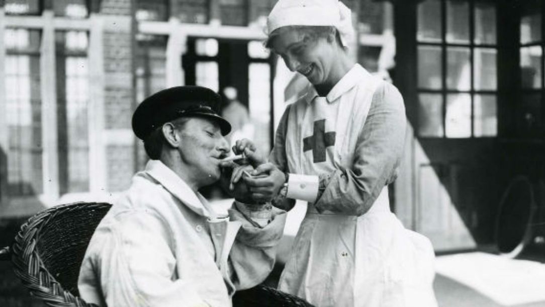 A black and white photograph showing a British Red Cross nurse lights cigarette for seated patient, as they both smile