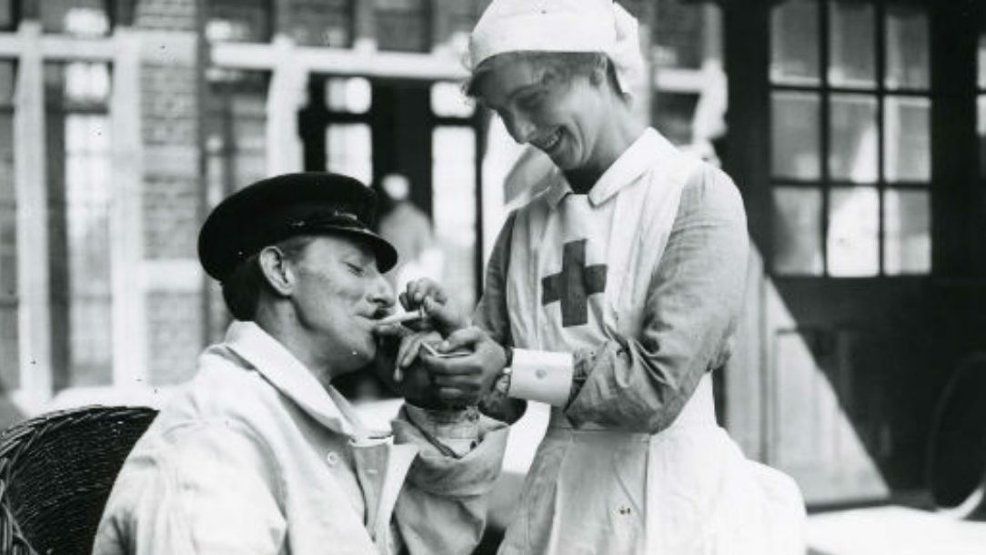 A black and white photograph showing a British Red Cross nurse lights cigarette for seated patient, as they both smile