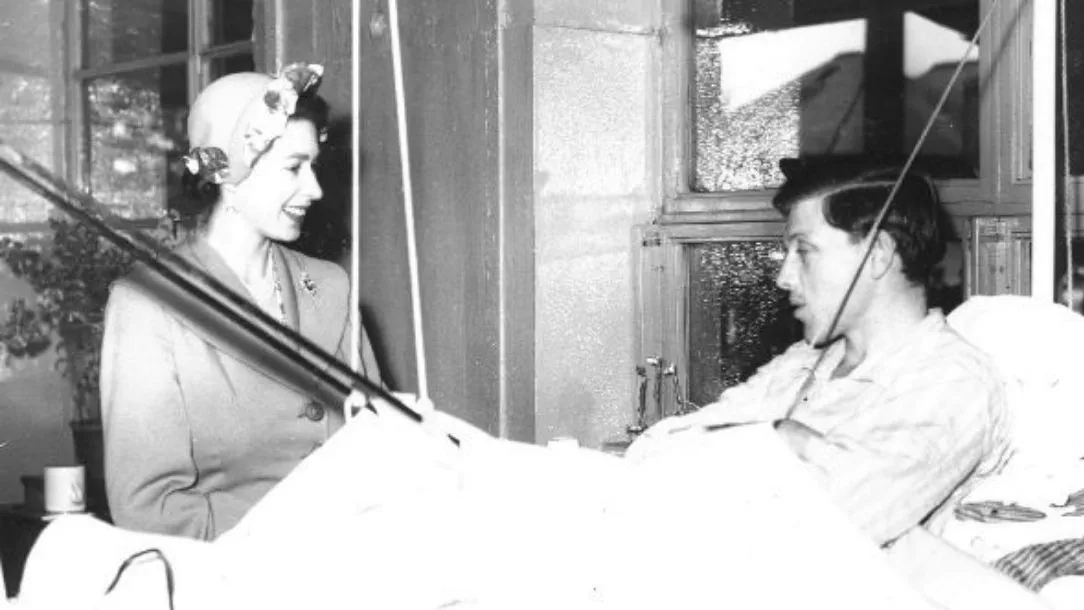A black and white photograph of smiling Queen Elizabeth II visiting an injured male service user.