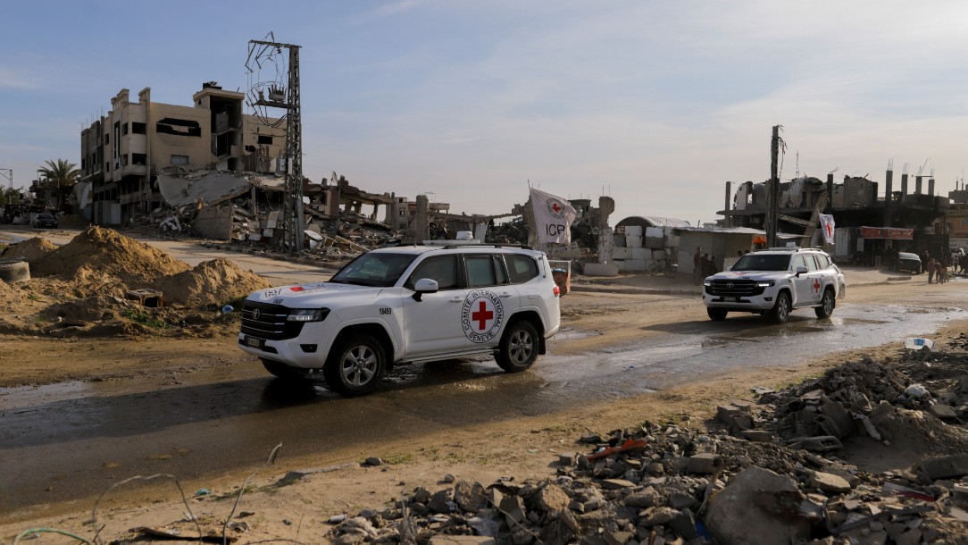 Vehicles emblazoned with the emblem of the International Committee of the Red Cross are seen driving in Gaza, with damaged buildings seen in the background