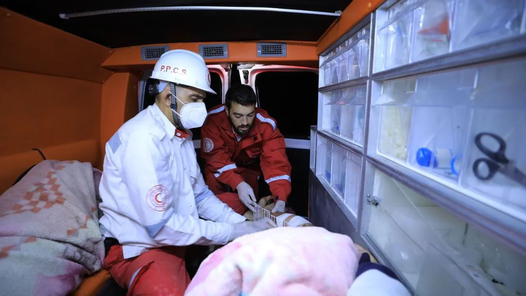 Two Palestine Red Crescent Society volunteers treat a patient inside an ambulance in Gaza.