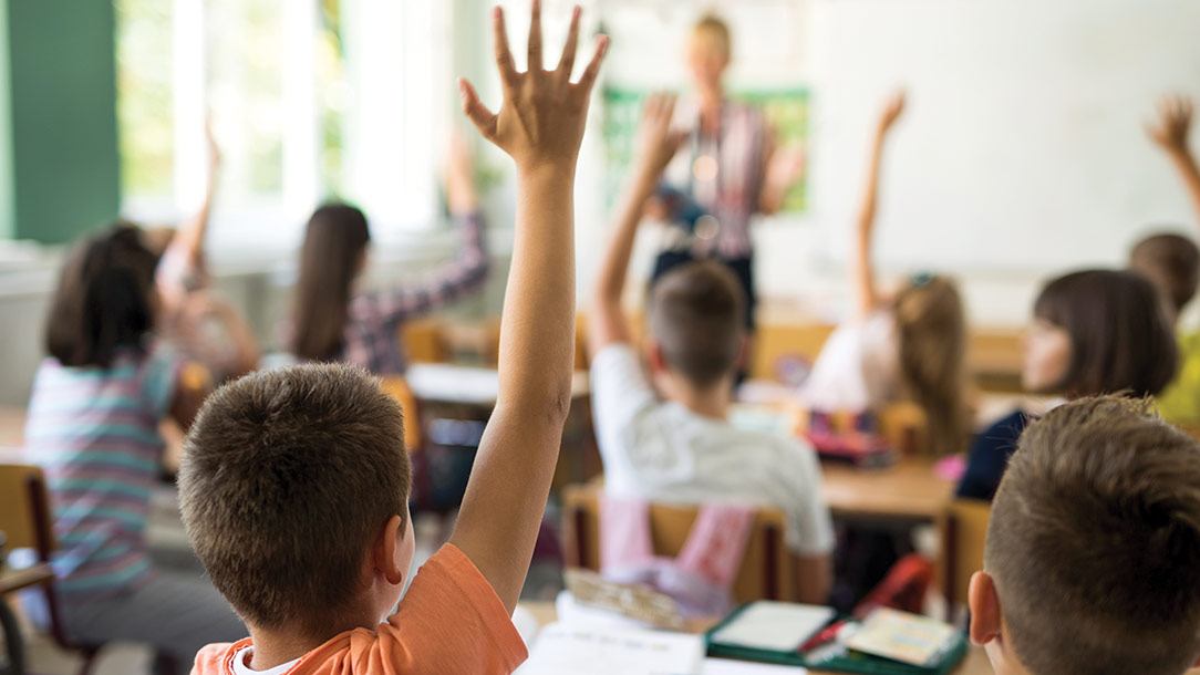 School children in classroom raise their hands.