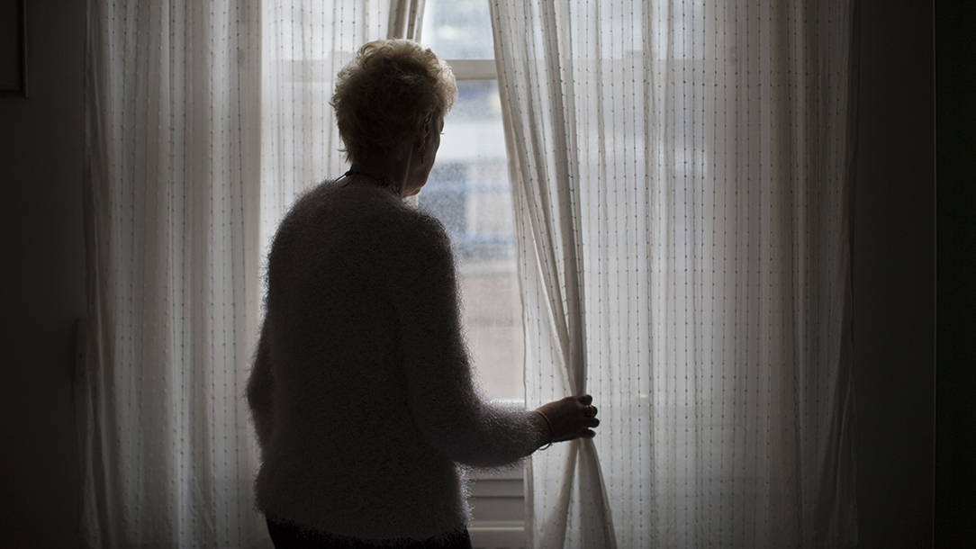 An older lady who is lonely looks out of the window.