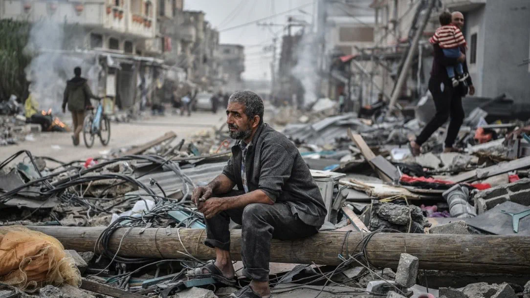 Man in Gaza sits in despair among destroyed buildings caused by conflict.