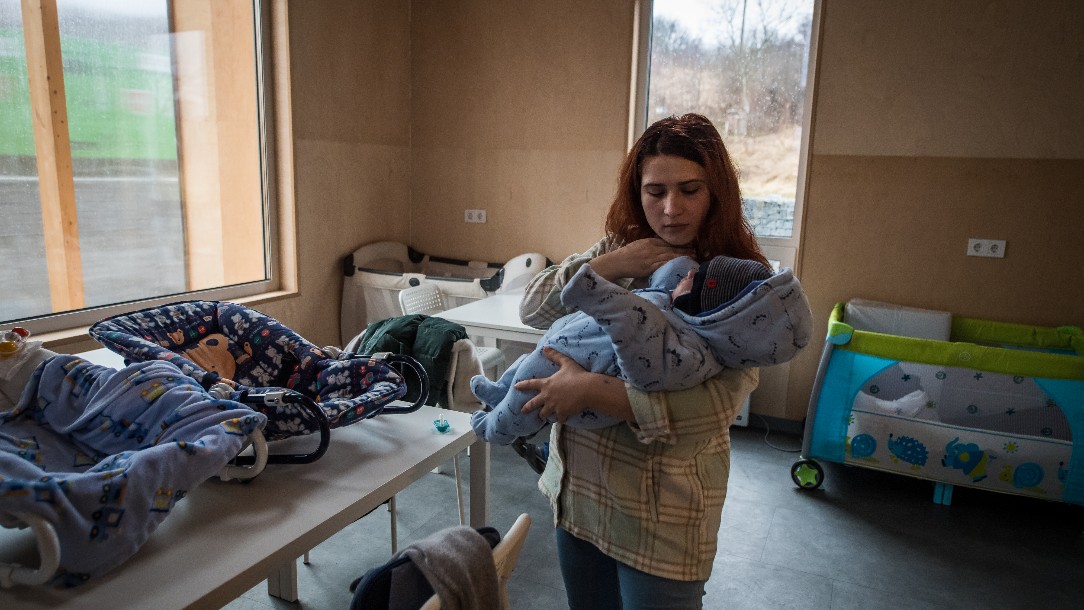 Margaryta holds her baby in the Unbroken Mothers centre in Lviv, Ukraine. The room is full of baby carriers and cots 