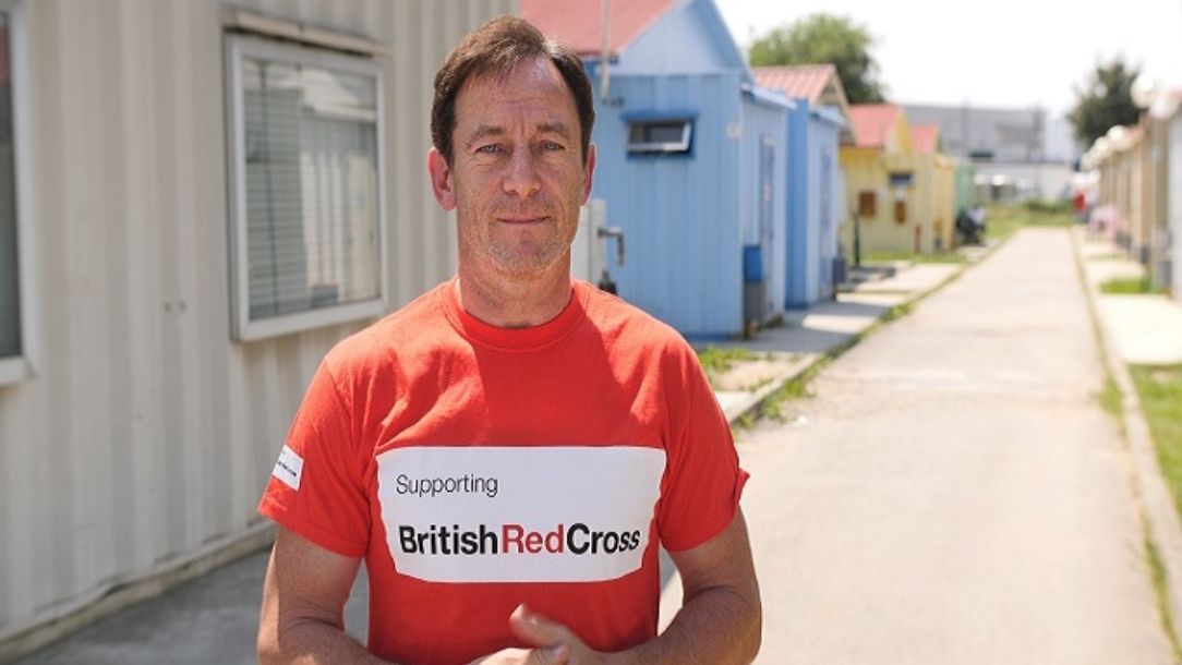 Jason Isaacs smiles for the camera in a British Red Cross t shirt.