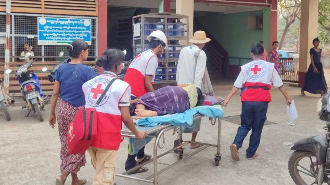 An injured person on a gurney is wheeled away by members of the Myanmar Red Cross Society