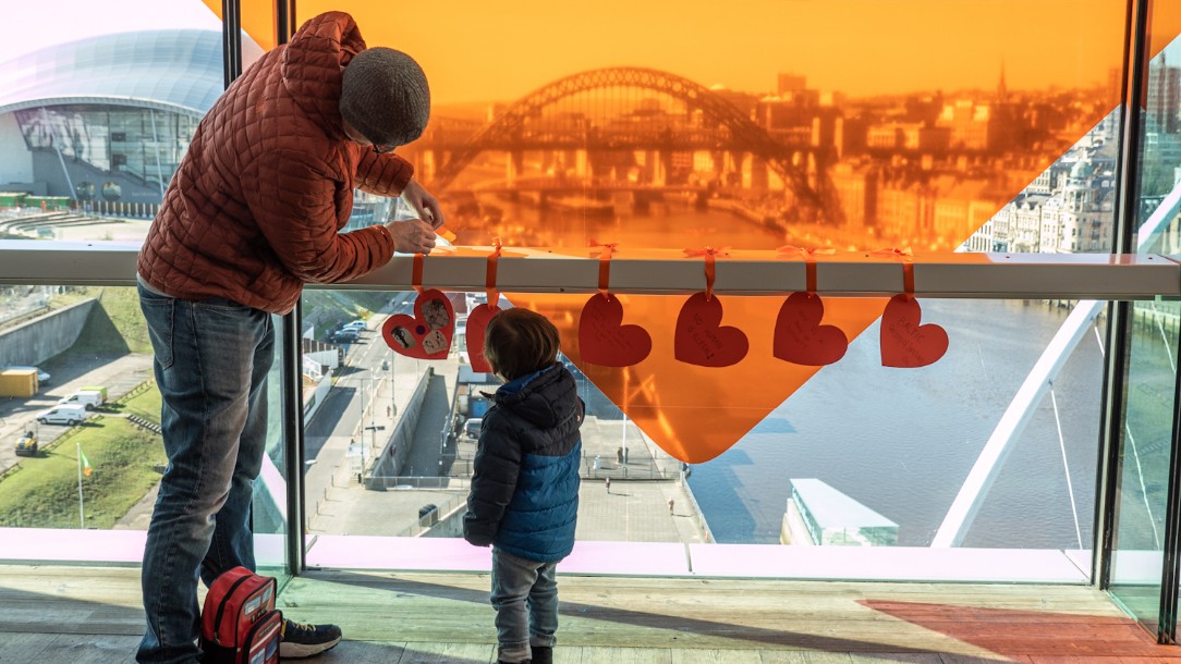 A man and child attach paper hearts saying 'Newcastle stands with refugees' to a railing overlooking the River Tyne in Newcastle 
