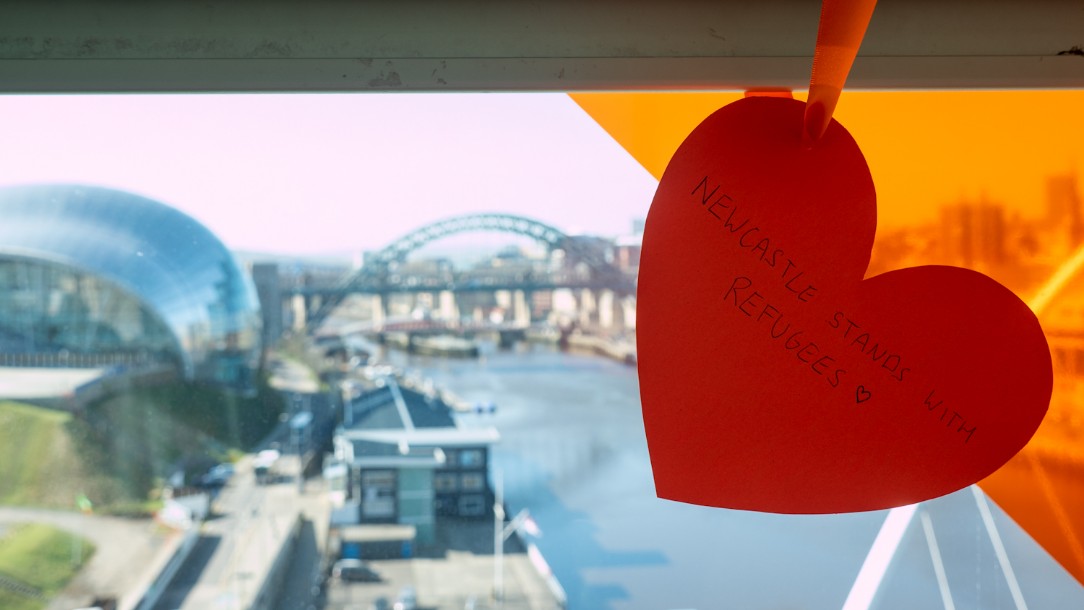 An orange heart which says 'Newcastle stands with refugees' hangs on a railing overlooking the River Tyne in Newcastle