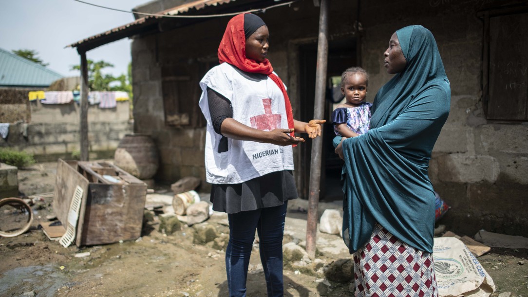 A Nigerian Red Cross volunteer talks to the mother of a child outside her home, which has been affected by flooding 