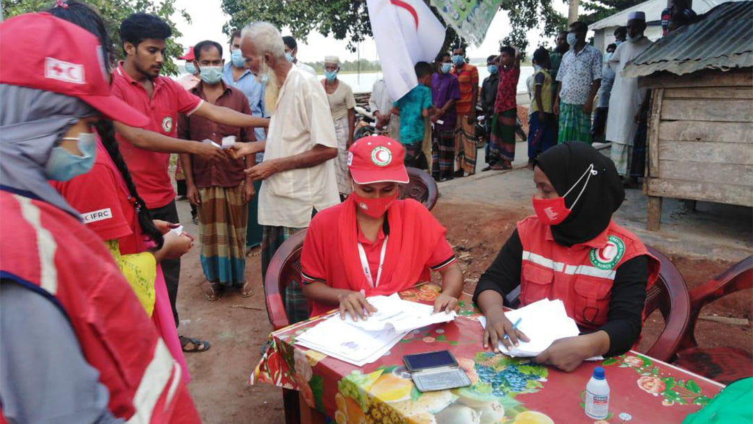 Red Cross partners the Bangladesh Red Crescent sit at a table giving people cash grants to prepare for a cyclone.