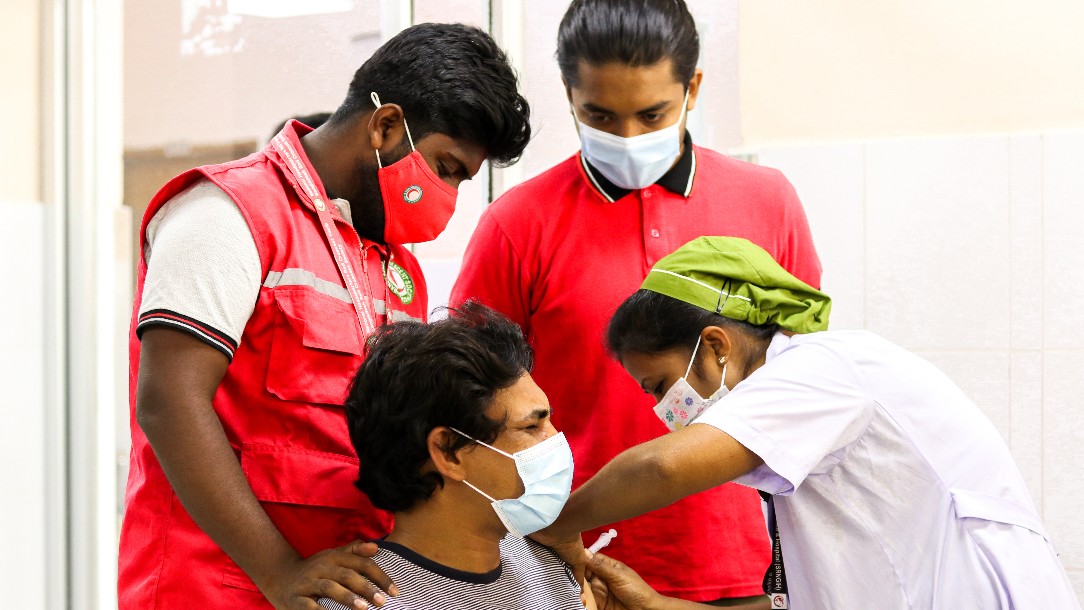 Volunteers stand with a man who is receiving his Covid-19 vaccination, in Bangladesh 
