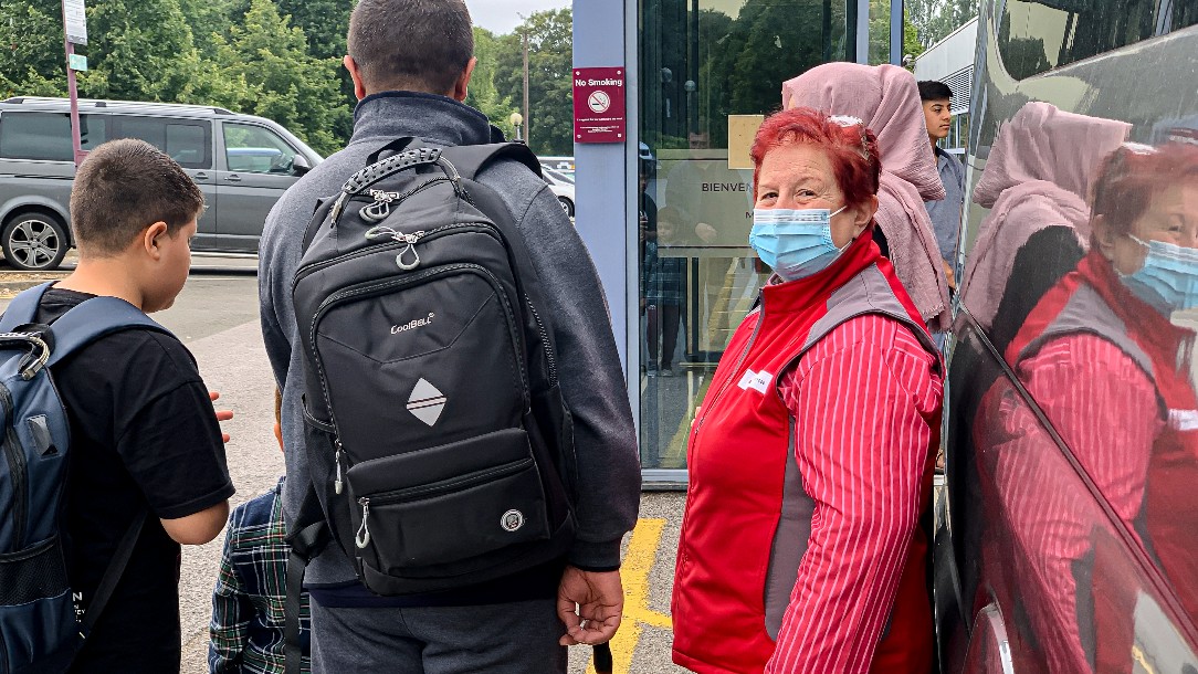 Emergency response officer Cathy, right, looks to camera wearing her Red Cross uniform, while helping people who have recently arrived from Afghanistan with their luggage