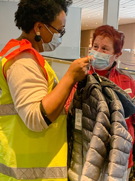 Refugee services manager Mekdes and emergency response officer Cathy stand together while holding an item of clothing that has been donated to families who have recently arrived from Afghanistan
