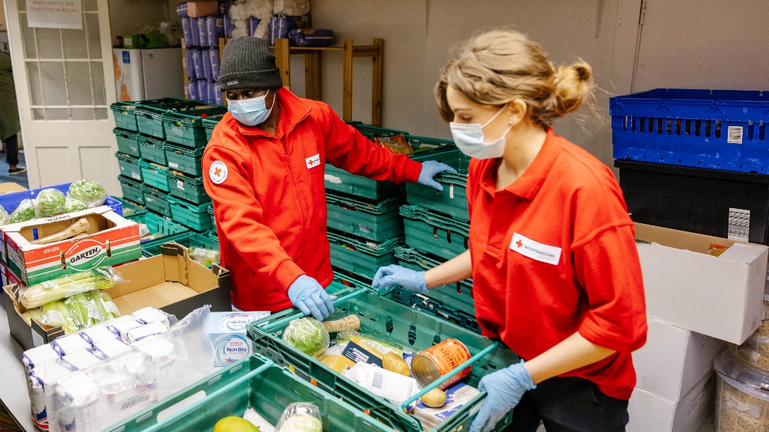 David and another volunteer pack up food parcels at the Hackney centre. Both are wearing Red Cross uniforms and face masks 