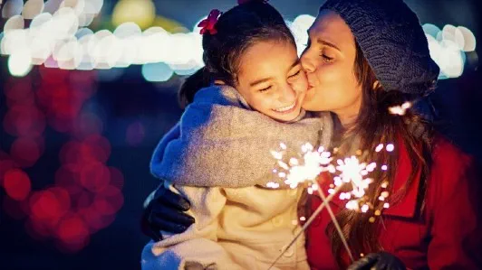 A mother hugs and kisses her daughter as they both hold sparklers.