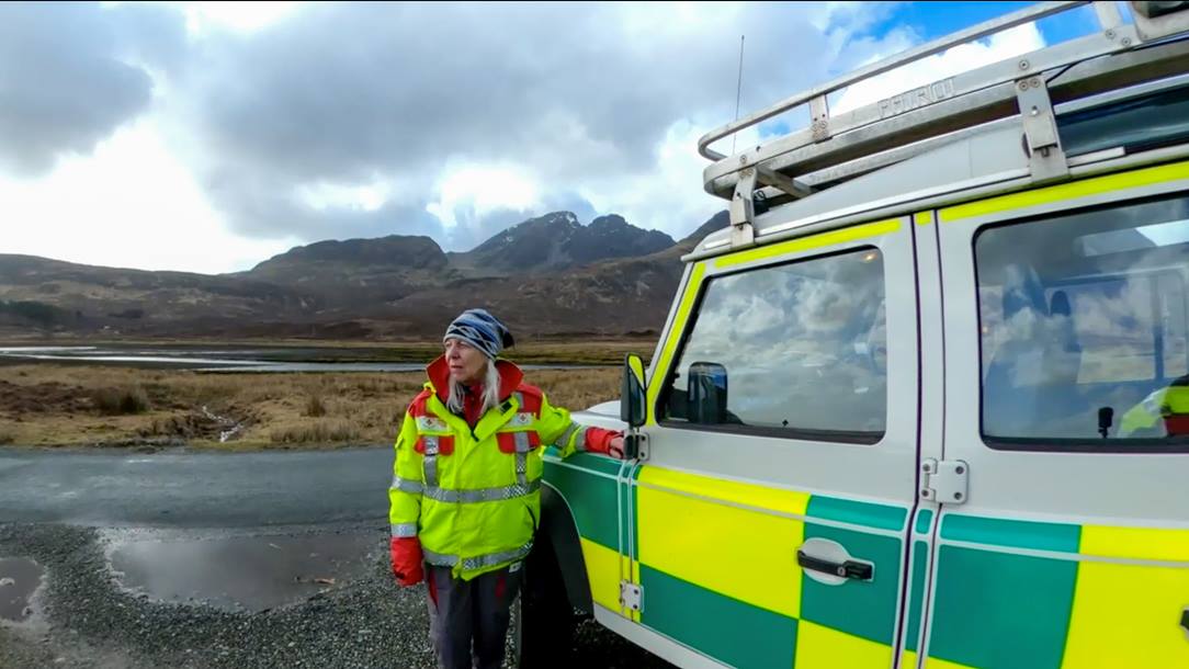 Volunteer Issie, wearing a face visor and her British Red Cross uniform, is seen stood beside a Land Rover vehicle, in a remote area of Scotland