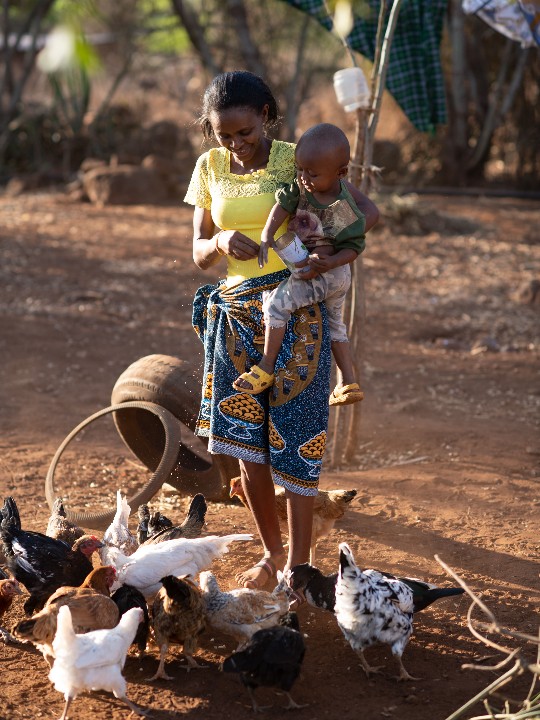 Jemimah holds her son, Bright, while watching over her chickens