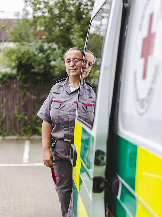 Kaye, a volunteer with our ambulance service, stands in her uniform next to a British Red Cross ambulance