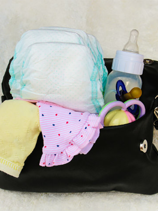 A nappy bag with nappies, a bottle, a dummy, a baby hat and a cloth.