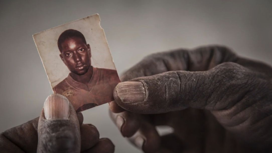 Two hands hold a small picture of a young man who left his home in Africa and is now missing.