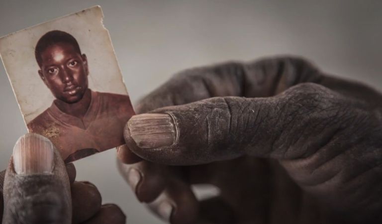 Hands hold a very small picture of a young man who left home in Africa and is now missing.