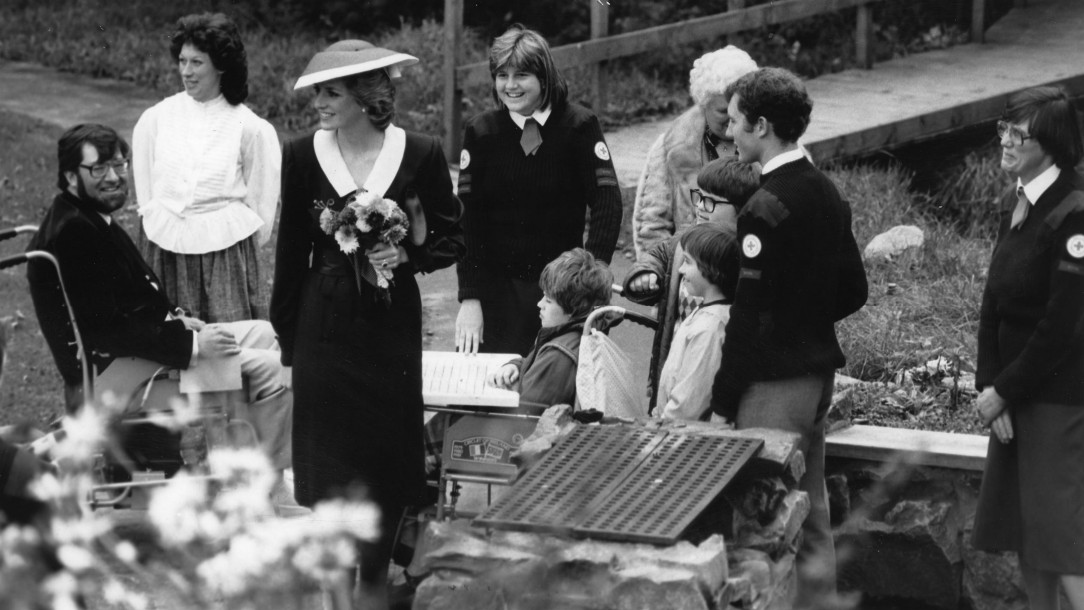 Princess Diana holds flowers and smiles at a group of adults and disabled children at a British Red Cross camp.