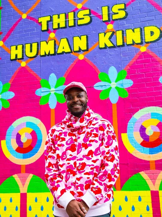 The artist Yinka Ilori stands in front of the mural he has designed for the British Red Cross. The mural reads 'This is human kind'