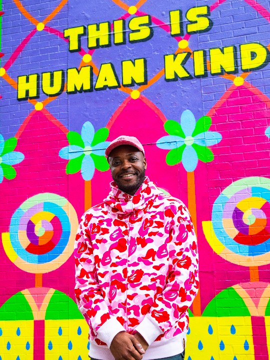 The artist Yinka Ilori stands in front of the mural he has designed for the British Red Cross. The mural reads 'This is human kind'