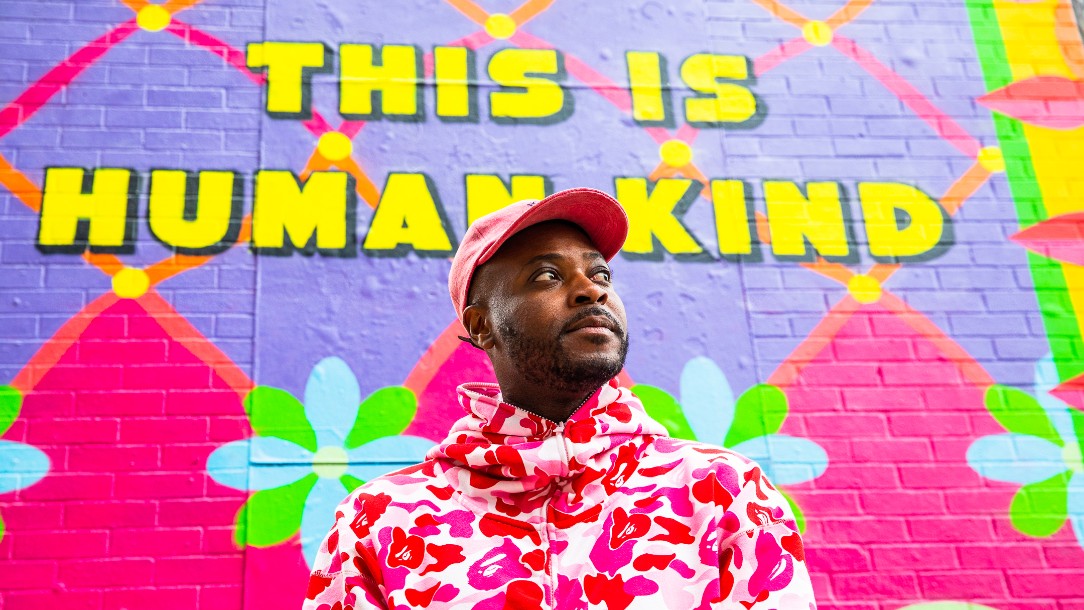 The artist Yinka Ilori stands in front of the mural he has designed for us, located in Shoreditch, East London. The mural reads 'This is human kind' 
