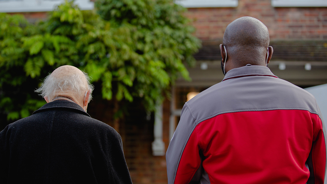 British Red Cross volunteer and older man photographed with their backs to the camera